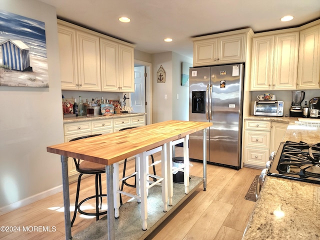 kitchen featuring butcher block countertops, light hardwood / wood-style floors, stainless steel appliances, and cream cabinetry