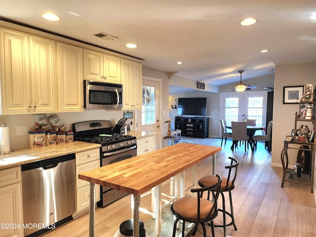 kitchen with appliances with stainless steel finishes, light stone counters, ceiling fan, light hardwood / wood-style flooring, and cream cabinetry