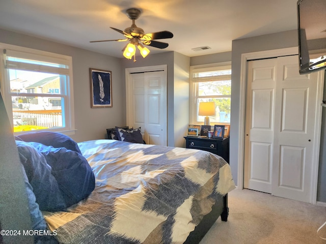 carpeted bedroom with ceiling fan, multiple closets, and multiple windows