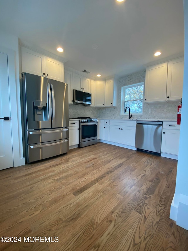 kitchen with sink, appliances with stainless steel finishes, tasteful backsplash, white cabinetry, and wood-type flooring