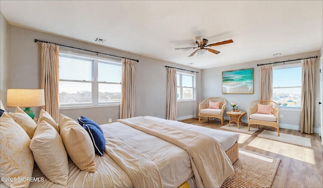 bedroom with a ceiling fan, visible vents, baseboards, and wood finished floors