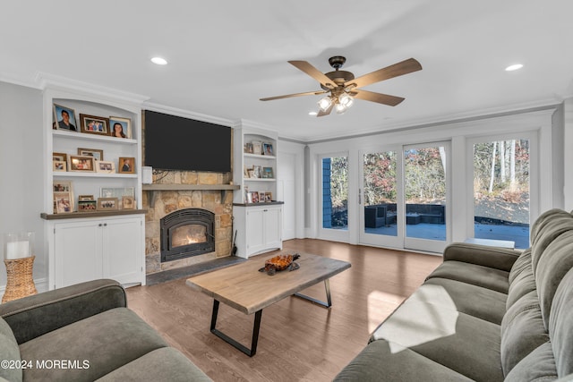 living room with ceiling fan, crown molding, built in features, light hardwood / wood-style flooring, and a stone fireplace