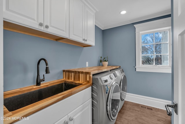 laundry room featuring cabinets, crown molding, sink, washer and dryer, and light hardwood / wood-style floors