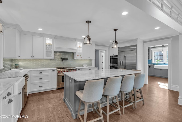 kitchen with hardwood / wood-style flooring, premium appliances, a kitchen island, a kitchen bar, and white cabinetry