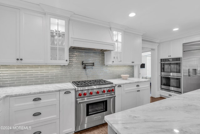 kitchen featuring light stone countertops, premium appliances, backsplash, white cabinets, and custom exhaust hood