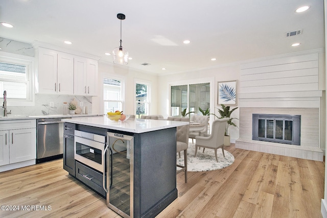 kitchen featuring light wood-type flooring, decorative light fixtures, white cabinetry, and stainless steel dishwasher