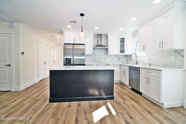 kitchen with decorative light fixtures, stainless steel appliances, light hardwood / wood-style flooring, and wall chimney range hood