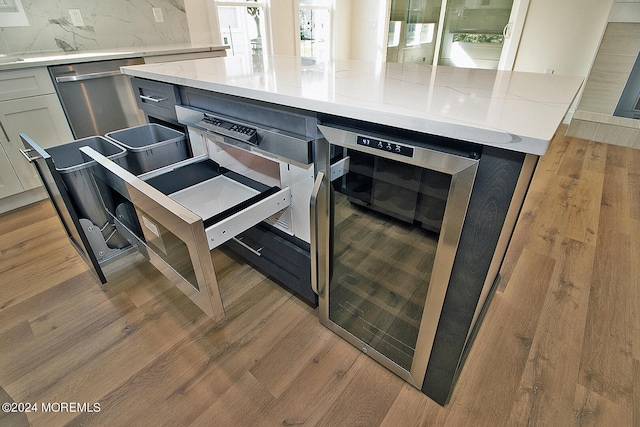 interior details featuring decorative backsplash, light stone counters, white cabinetry, light hardwood / wood-style flooring, and wine cooler