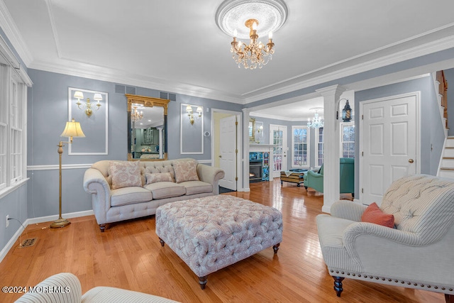 living room featuring ornate columns, a chandelier, ornamental molding, and light wood-type flooring