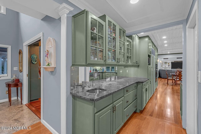 bar featuring light wood-type flooring, dark stone counters, green cabinets, and sink