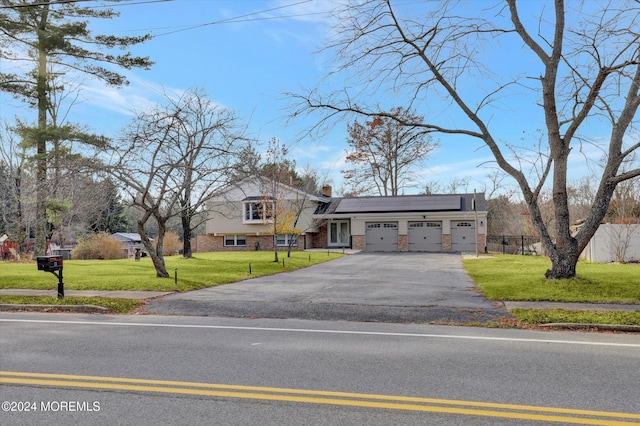 tri-level home with solar panels, a garage, and a front yard