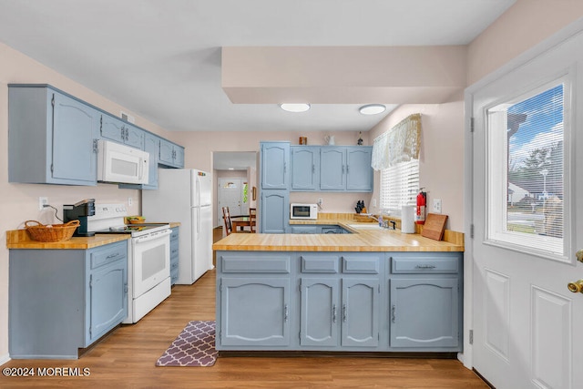 kitchen with kitchen peninsula, light wood-type flooring, white appliances, and blue cabinetry