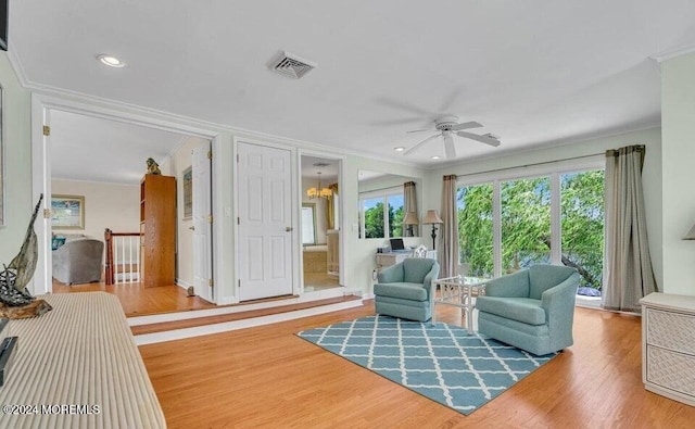 living area with ceiling fan with notable chandelier, wood-type flooring, and crown molding