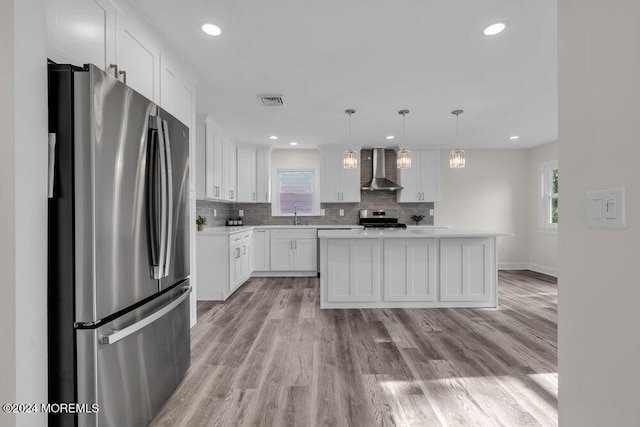 kitchen with white cabinetry, wall chimney range hood, decorative light fixtures, a kitchen island, and appliances with stainless steel finishes