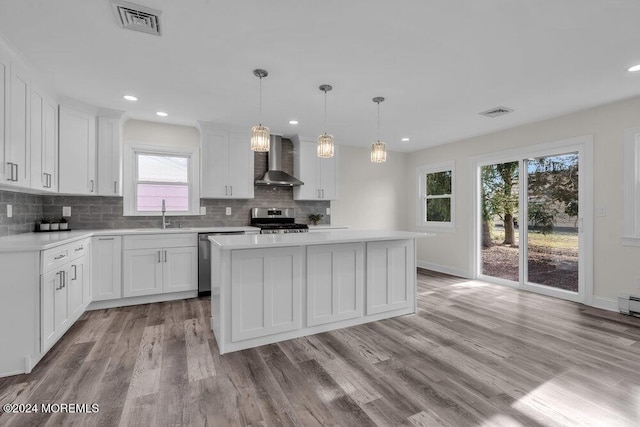 kitchen featuring white cabinetry, wall chimney exhaust hood, hanging light fixtures, stainless steel appliances, and light wood-type flooring