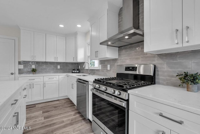 kitchen with wall chimney exhaust hood, light wood-type flooring, white cabinetry, and stainless steel appliances