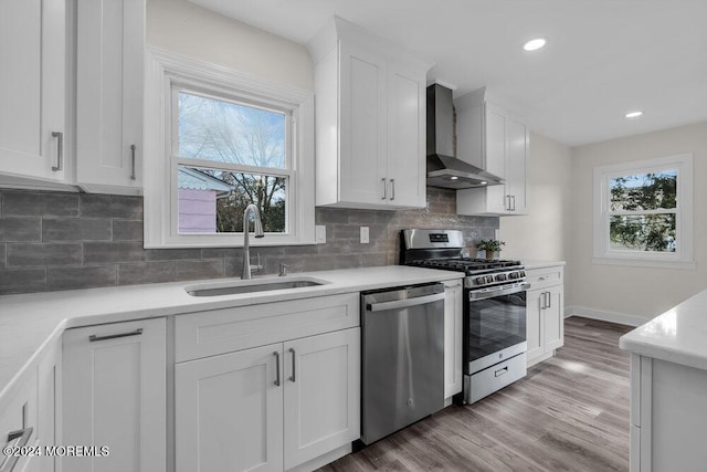 kitchen featuring stainless steel appliances, sink, wall chimney range hood, white cabinets, and light hardwood / wood-style floors