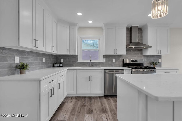 kitchen featuring pendant lighting, white cabinets, wall chimney range hood, sink, and appliances with stainless steel finishes