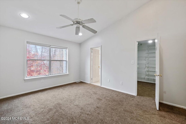 unfurnished bedroom with dark colored carpet, a spacious closet, ceiling fan, and lofted ceiling