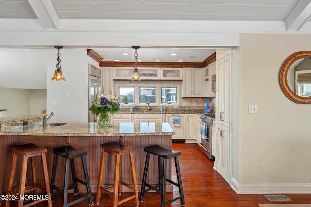 kitchen with beam ceiling, light stone counters, dark hardwood / wood-style flooring, a breakfast bar area, and appliances with stainless steel finishes