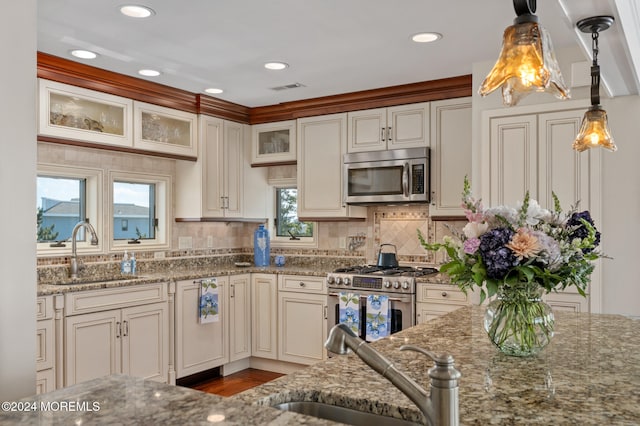 kitchen featuring sink, light stone counters, stainless steel appliances, and hanging light fixtures