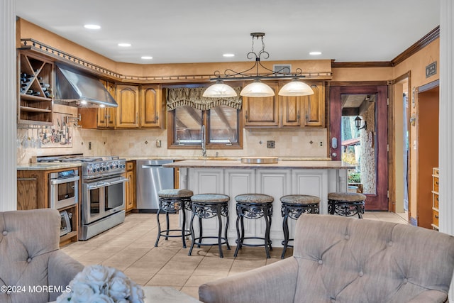 kitchen featuring a center island, wall chimney exhaust hood, light tile patterned floors, appliances with stainless steel finishes, and decorative light fixtures