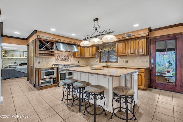 kitchen featuring a center island, stainless steel appliances, wall chimney range hood, crown molding, and light tile patterned floors