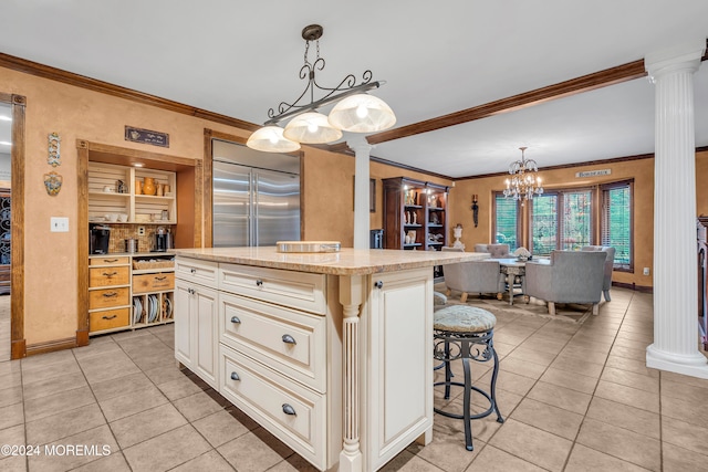 kitchen with built in refrigerator, ornate columns, light tile patterned floors, decorative light fixtures, and a kitchen island