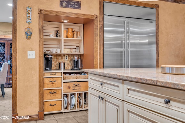 kitchen featuring white cabinets, stainless steel built in fridge, light stone countertops, and light tile patterned floors