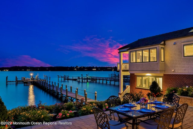 patio terrace at dusk featuring a water view and a dock