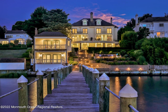 back house at dusk featuring a balcony and a water view