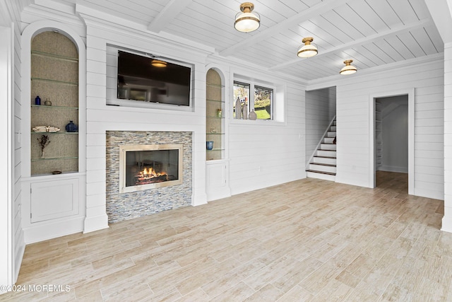 unfurnished living room featuring wood walls, wooden ceiling, a tile fireplace, beam ceiling, and light hardwood / wood-style floors