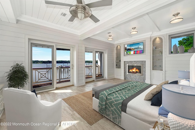 bedroom featuring access to outside, a stone fireplace, wood walls, and light hardwood / wood-style flooring