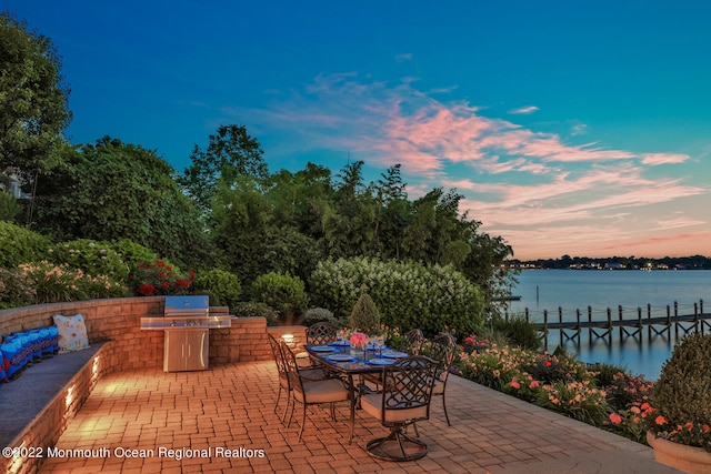 patio terrace at dusk featuring area for grilling, a water view, and grilling area