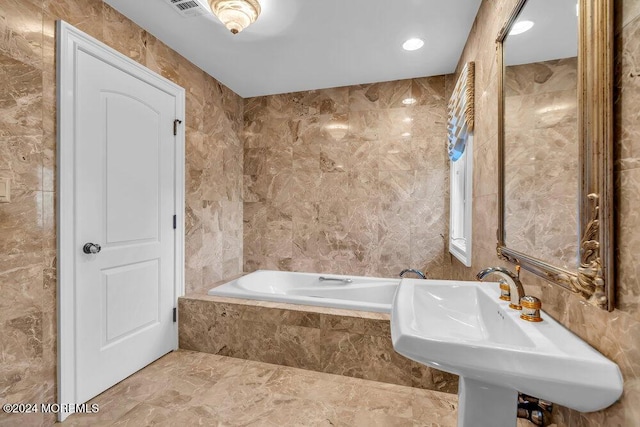 bathroom with tiled tub, sink, and tile walls