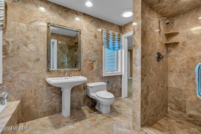 bathroom with sink, tiled shower, toilet, and tile walls