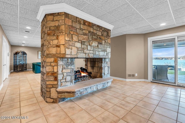 living room with a paneled ceiling, a stone fireplace, a water view, and light tile patterned floors