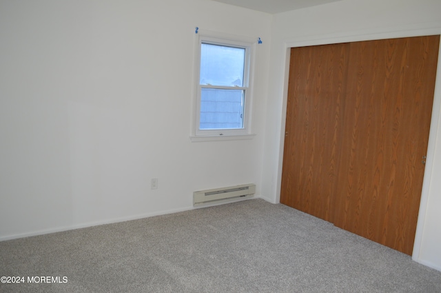 unfurnished bedroom featuring carpet flooring, a closet, and a baseboard heating unit