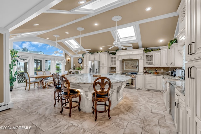 kitchen featuring light stone counters, stainless steel appliances, ceiling fan, a spacious island, and white cabinets