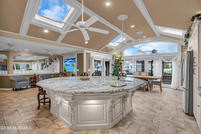 kitchen featuring light stone countertops, stainless steel fridge, a skylight, a spacious island, and white cabinetry