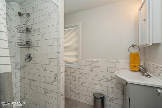 bathroom featuring tile patterned floors, vanity, a tile shower, and tile walls