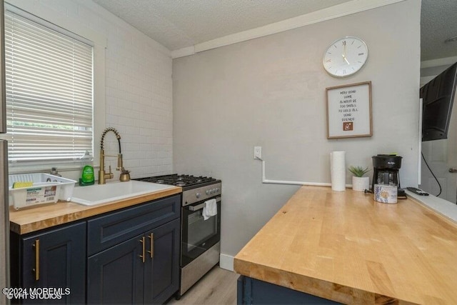 kitchen with wooden counters, a textured ceiling, stainless steel gas range oven, and sink