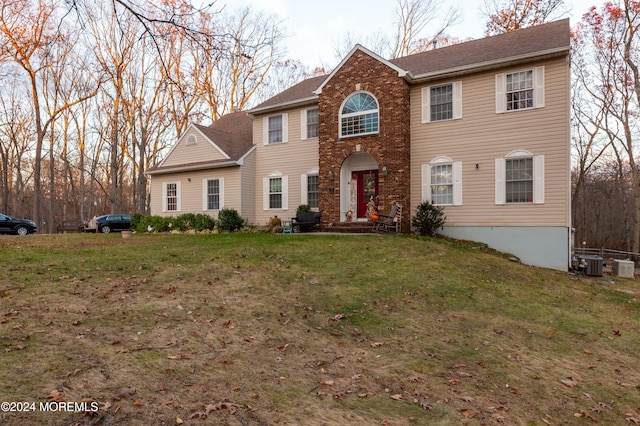 colonial-style house featuring central AC and a front lawn