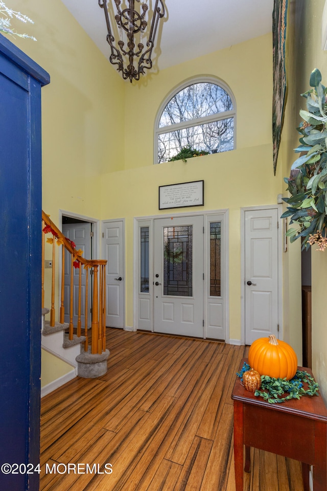 foyer entrance featuring a towering ceiling, hardwood / wood-style flooring, and a notable chandelier