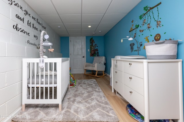 bedroom with a drop ceiling, light hardwood / wood-style floors, and a nursery area