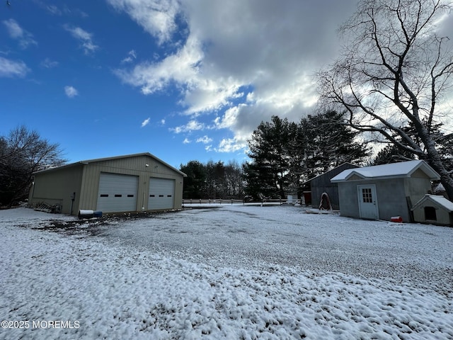 yard layered in snow featuring a garage and an outbuilding