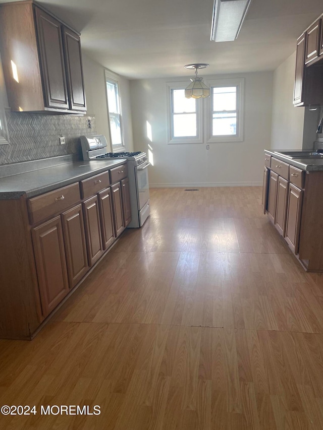 kitchen featuring gas range, dark brown cabinetry, sink, wood-type flooring, and decorative backsplash