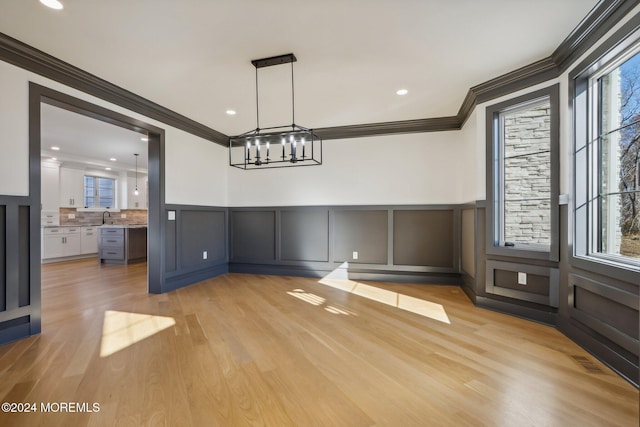 unfurnished dining area with a chandelier, sink, ornamental molding, and light wood-type flooring