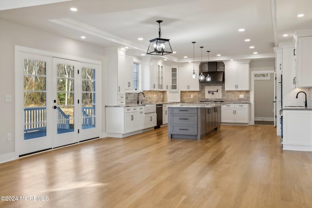 kitchen with light wood-type flooring, wall chimney range hood, white cabinets, a center island, and hanging light fixtures