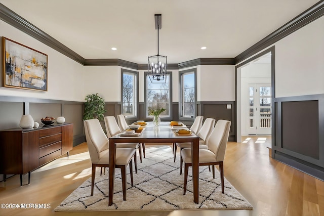 dining space with light hardwood / wood-style floors, ornamental molding, and a notable chandelier